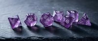 Polished amethyst gemstone dice set with white numbers for tabletop gaming, role-playing games, and dungeon adventures on dark slate surface.