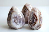 Polished agate crystal eggs displaying natural banded patterns and geode formations in soft gray and brown tones against white background, mineral collection piece.