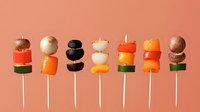 Colorful appetizer canapes on wooden skewers arranged in row on coral background. Creative party food styling for catering and events.