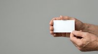 Senior male hands holding blank white business card against neutral gray background for branding and corporate identity mockups.