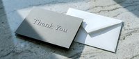 Elegant gray thank you card with white envelope on marble surface, soft natural light creating a sophisticated, minimalist stationery scene.