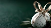 Elegant white Christmas ornament with gold ribbon and polka dot pattern on dark green background, perfect for holiday decorations.