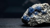 Blue sodalite mineral crystals embedded in white matrix rock specimen on dark background for geology education and gemstone collection displays.