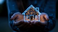 Glowing house silhouette with fairy lights floating between cupped hands against dark background, creating magical home concept for real estate and protection.