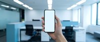 Caucasian male hand holding smartphone with blank white screen in modern office environment with blue partitions and natural lighting.