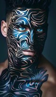 Young male model with artistic black and blue tribal face paint design against dark background, featuring intense blue eyes and dramatic makeup patterns for fashion editorial.