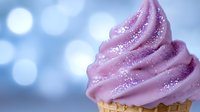 Pink swirled soft serve ice cream or frosting topped with sparkly sugar crystals in waffle cone against dreamy blue bokeh background. Sweet dessert macro photography.