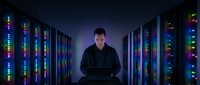 Caucasian male IT specialist working on laptop in modern data center server room with colorful LED lights creating futuristic technology atmosphere.