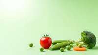 Fresh organic vegetables including red tomato, green peas, broccoli and carrot arranged on light green gradient background for healthy eating concepts.