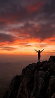 Silhouette of person with raised arms celebrating success on mountain peak at dramatic sunset with orange and purple clouds over valley landscape.