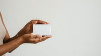 Dark-skinned hand holding blank white box against neutral background, suitable for product packaging mockups, branding, and commercial advertising campaigns.