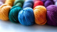 Colorful yarn balls in vibrant rainbow colors arranged in row on white background. Close-up macro shot showing detailed texture of wool threads for knitting and crafting projects.