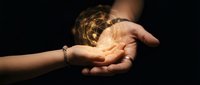 Hands holding glowing golden light orb with magical energy rays against dark background for spiritual healing and mystical concepts.