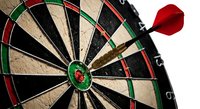 Red dart hitting bullseye center of traditional dartboard game target with numbered segments for precision sports competition and recreational entertainment.