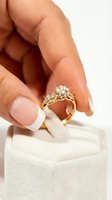Woman's hand with French manicure holding a sparkling diamond gold engagement ring above a velvet jewelry box, close-up shot.