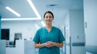 Female healthcare professional in teal scrubs standing confidently in modern hospital corridor with fluorescent lighting, suitable for medical, healthcare, and clinical industry content.