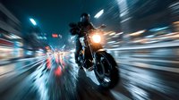 Motorcyclist racing through city streets at night with dramatic motion blur and neon lights creating dynamic speed trails and urban atmosphere.
