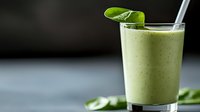 Fresh green smoothie with spinach leaf garnish in tall glass on dark background, healthy breakfast drink with natural ingredients and vitamins.