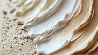Creamy white cosmetic texture with smooth swirls and droplets on textured surface for skincare and beauty product applications.