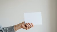 Mature adult hand holding blank white card against neutral background for messaging or branding purposes.