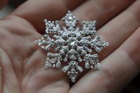 Sparkling crystal snowflake brooch with intricate details resting in palm of hand, featuring delicate silver metalwork and clear gemstone accents in winter design.