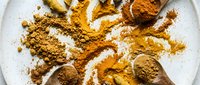 Turmeric and various spice powders scattered on white ceramic plate, overhead flat lay composition for culinary and wellness content.