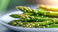 Fresh green asparagus spears drizzled with olive oil and seasonings on white ceramic plate, macro view showing texture and natural sheen in soft lighting.