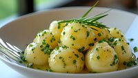 Fresh boiled baby potatoes garnished with melted butter, chopped chives, and herbs served on white plate, close-up view showing texture and glossy surface.