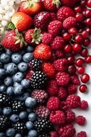 Fresh mixed berries arranged in diagonal pattern including strawberries, raspberries, blackberries, blueberries and cranberries on white background. Food photography.