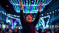 Joyful child raising hands under colorful bokeh Christmas lights at night, celebrating festive holiday season outdoors.