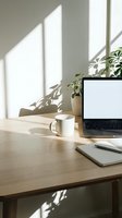 Minimalist home office workspace with laptop, coffee mug and notebook on wooden desk near window with natural sunlight and plant shadows for remote work.
