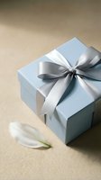 Elegant light blue gift box with silver satin ribbon bow and white feather on neutral beige background for special occasions and celebrations.