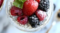 Fresh berries and chia seeds layered with creamy yogurt in glass bowl, macro view showing texture of strawberries, blackberries and raspberries dusted with sugar.