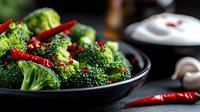 Fresh broccoli stir-fry with red chili peppers in black pan, healthy vegetable dish for cooking and nutrition content.