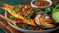 Grilled whole fish with fresh herbs, chili peppers and lime garnish served on white platter. Traditional seafood dish with colorful vegetables and spicy sauce.