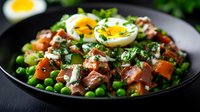 Fresh salad with tender meat chunks, soft-boiled eggs, green peas, tomatoes and herbs served on black plate, close up view of healthy protein-rich meal.