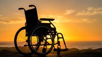 Silhouette of empty wheelchair on beach at sunset with golden sky and ocean horizon, symbolizing accessibility and independence.