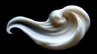 Creamy white swirl of cosmetic product on black background, showcasing smooth texture and elegant curve for skincare advertising.