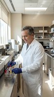 Middle-aged Caucasian male scientist in white lab coat working with test tubes in modern laboratory. Professional researcher conducting experiments in clinical setting.