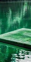 Serene emerald green lake water with stone platform edge creating peaceful reflections and ripples. Minimalist composition for meditation and wellness concepts.