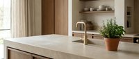 Minimalist kitchen interior with light marble countertop, wooden cabinetry, brass faucet, potted plant, and open shelving for home design and renovation projects.