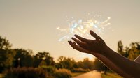 Hands releasing glowing magical light particles at golden sunset creating mystical energy flow in nature landscape for spiritual wellness concepts.