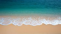 Gentle ocean waves washing up on pristine sandy beach with turquoise blue water creating natural pattern of white foam on golden sand shoreline.