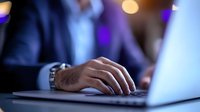 Male hand typing on laptop keyboard in dark office environment with blurred purple and golden bokeh lights in background, business professional at work late hours.