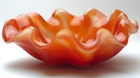 Wavy orange glass bowl with ruffled edges and translucent gradient design on white background, modern decorative art piece for contemporary home decor.