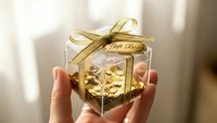 Hands holding transparent gift box with golden ribbon containing luxury present for special occasions and celebrations.