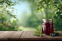 Homemade blackberry jam in glass jar on rustic wooden table with fresh berries and green foliage in blurred garden background.