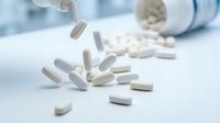 White and gray capsule pills spilling from an open bottle onto a clean surface, representing medication, pharmaceuticals, and healthcare treatment options.