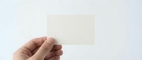 Hand holding blank cream colored card or paper against white background, isolated mockup for business branding, stationery design, and marketing materials.