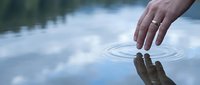 Hand touching calm water surface creating ripples with reflection, peaceful meditation and mindfulness concept for wellness and tranquility themes.